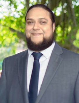 Alejandro in the nature wearing a grey suit smiling at the camera