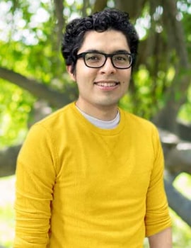 Felix in the nature wearing yellow sweater smiling at the camera