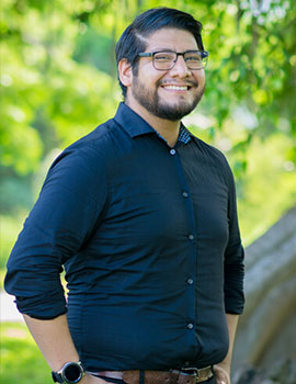 Fernando in the nature with his hands in his pockets smiling at the camera