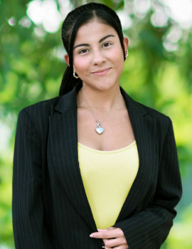 Jesica in the nature wearing black suit and yellow sweater smiling at the camera