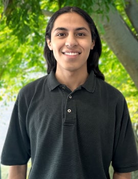 Zhadyd in the nature with long hair and black t-shirt smiling at the camera